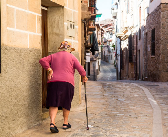 Mujer mayor caminando con bastón por el barrio, participando en actividades comunitarias para prevenir la soledad no deseada